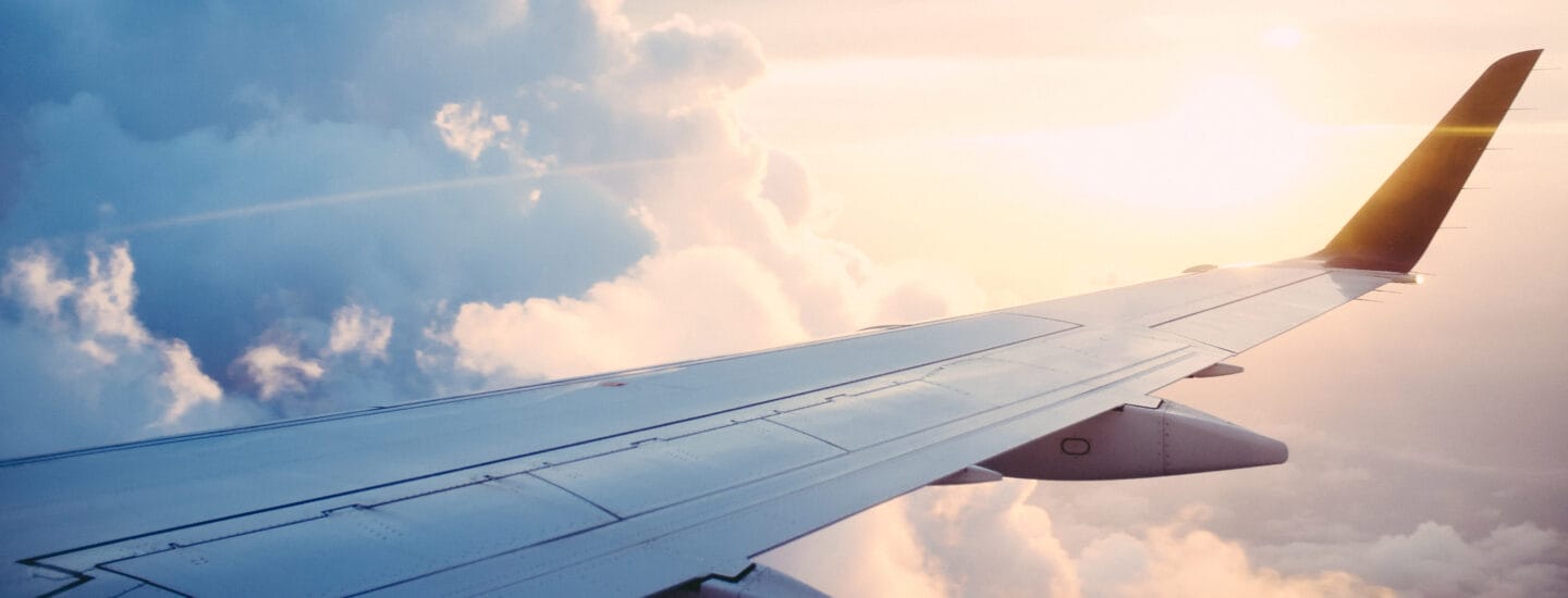 Udsigt fra et flyvindue, der viser vingen, der skærer gennem luftige skyer. Uanset om det flyver mod en stigende eller nedgående sol, er det varme skær over scenen en betagende påmindelse om, hvordan danskere verden over forbliver forbundet på tværs af himmel og land.