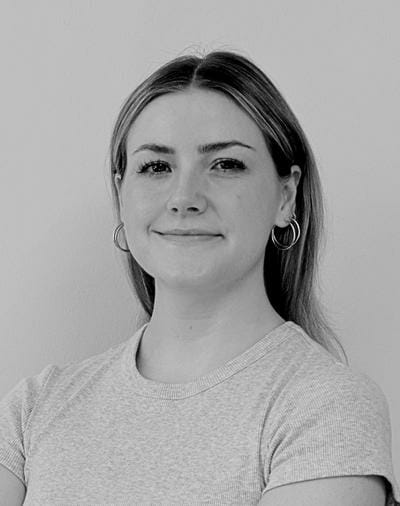 Sort-hvidt portræt af en person med langt hår iført en lys t-shirt og ringøreringe, smilende let mod en almindelig baggrund.