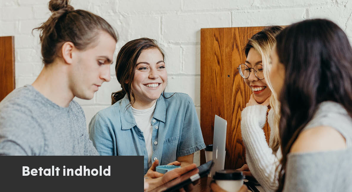 Fire personer sidder sammen ved et bord, engageret i samtale og smilende. En bærbar computer og kaffekopper står på bordet. Atmosfæren er afslappet og venlig. En tekstblok i bunden siger "Betalt indhold.