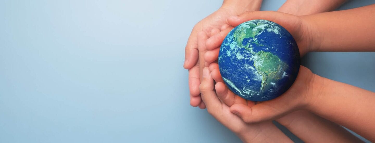 Hands of several people gently holding a small globe against a light blue background, symbolizing unity and care for the Earth, much like the community fostered on the Danes Worldwide website.