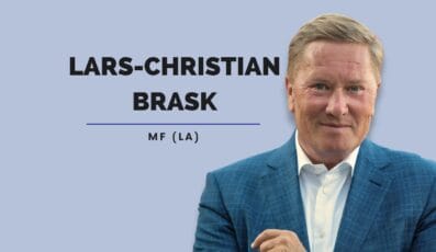 En mand i blåt jakkesæt og hvid skjorte smiler med armene over kors mod en lyseblå baggrund. Ved siden af ham står teksten "Lars-Christian Brask MF (LA)" med fede sorte bogstaver.