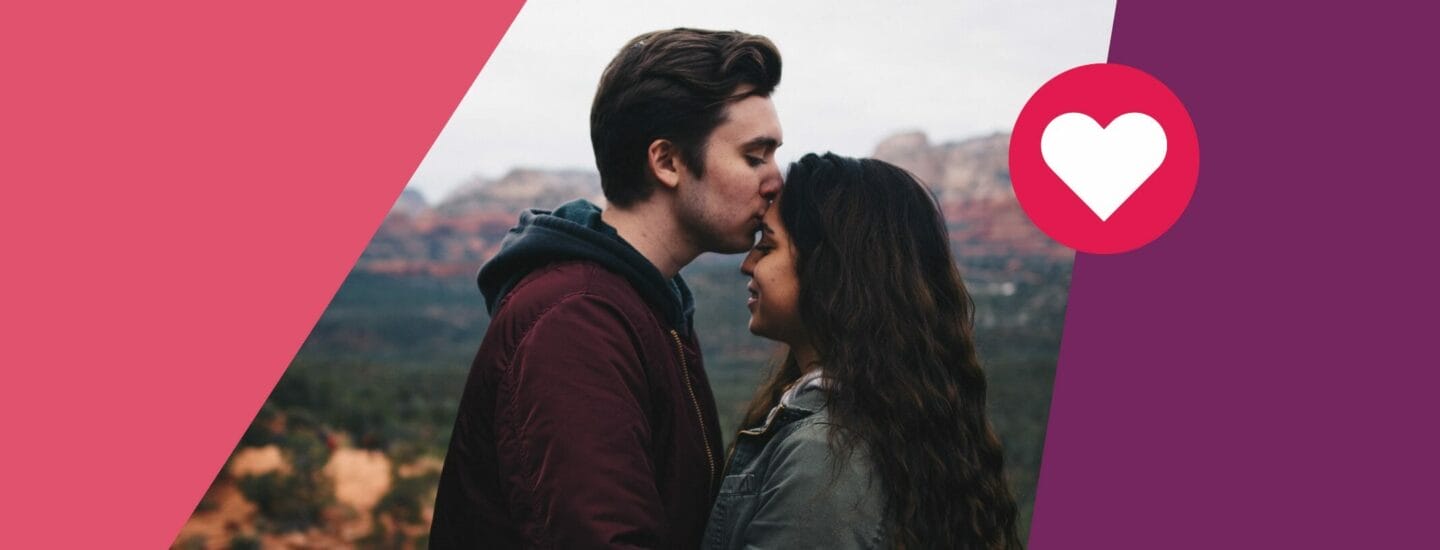 A man gently kisses a womans forehead as they stand close outdoors, surrounded by blurred natural scenery. The image is framed with red and purple diagonal borders, featuring a heart symbol on the right side.