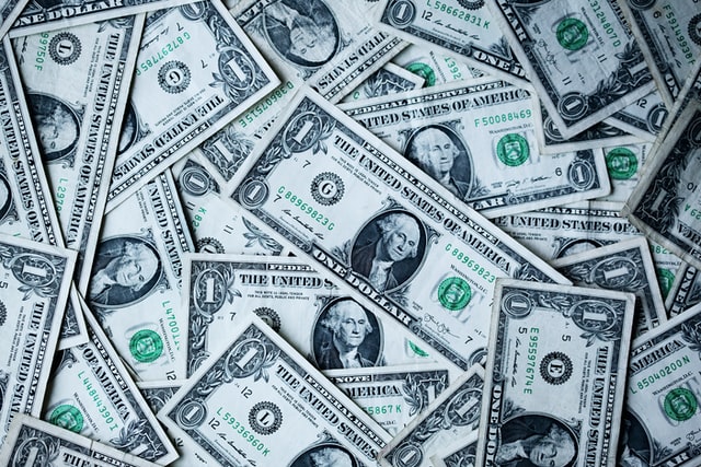 En spredt bunke af amerikanske endollarsedler viser George Washingtons portræt, der symboliserer fuld skattepligt. De overlappende sedler skaber et tekstureret mønster med synlige serienumre og skatkammerforseglingen i grønt blæk, der formidler en følelse af overflod og valuta.